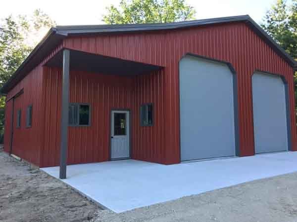 Red metal building with gray garage doors and a concrete pad.