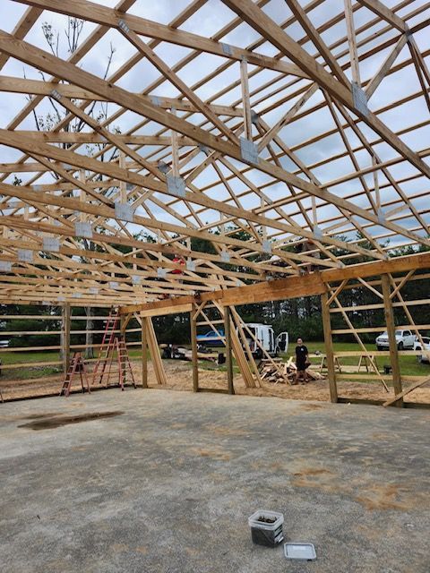 Wooden frame of a building under construction, exterior view. Workers and equipment are visible.