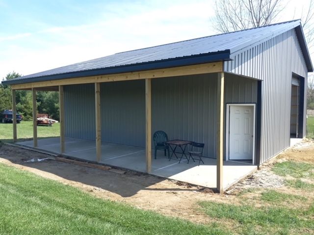 Metal shed with a covered porch area. Gray siding, black roof, and concrete pad.