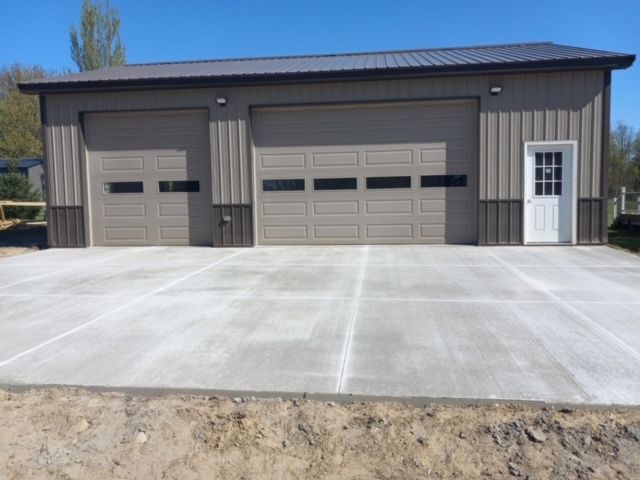 Tan garage with two doors and a white door on a concrete slab, blue sky.