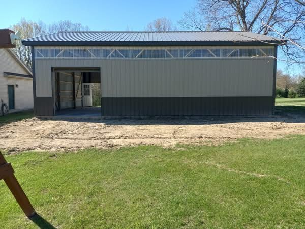 A large, two-tone metal building with a garage door open on a grassy lawn.