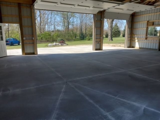 Inside of a garage with large open doors facing a grassy area; concrete floor, beams, and open doorway.
