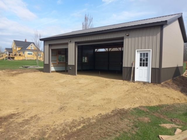 Tan and brown metal garage with open bays, white door, and gravel driveway.
