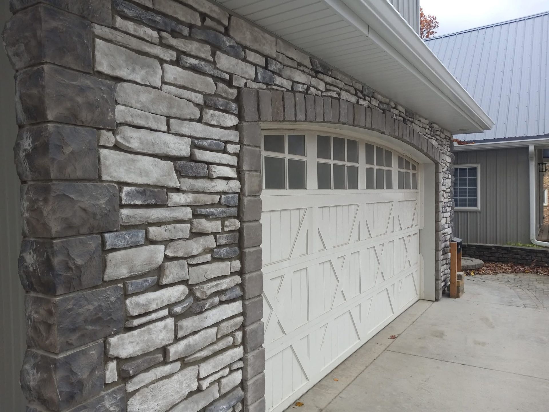 Stone facade on a garage. Gray and brown stone with a white garage door.