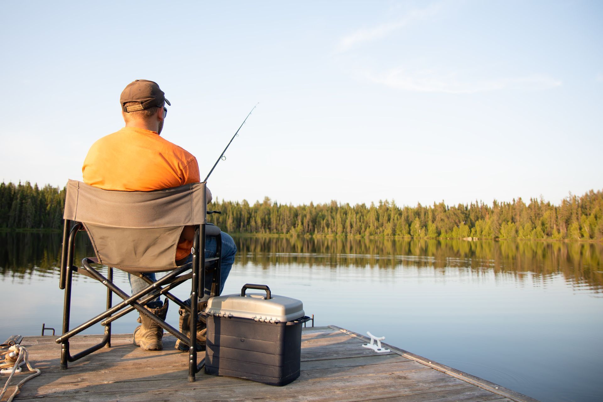 A man is sitting on a dock fishing on a lake.