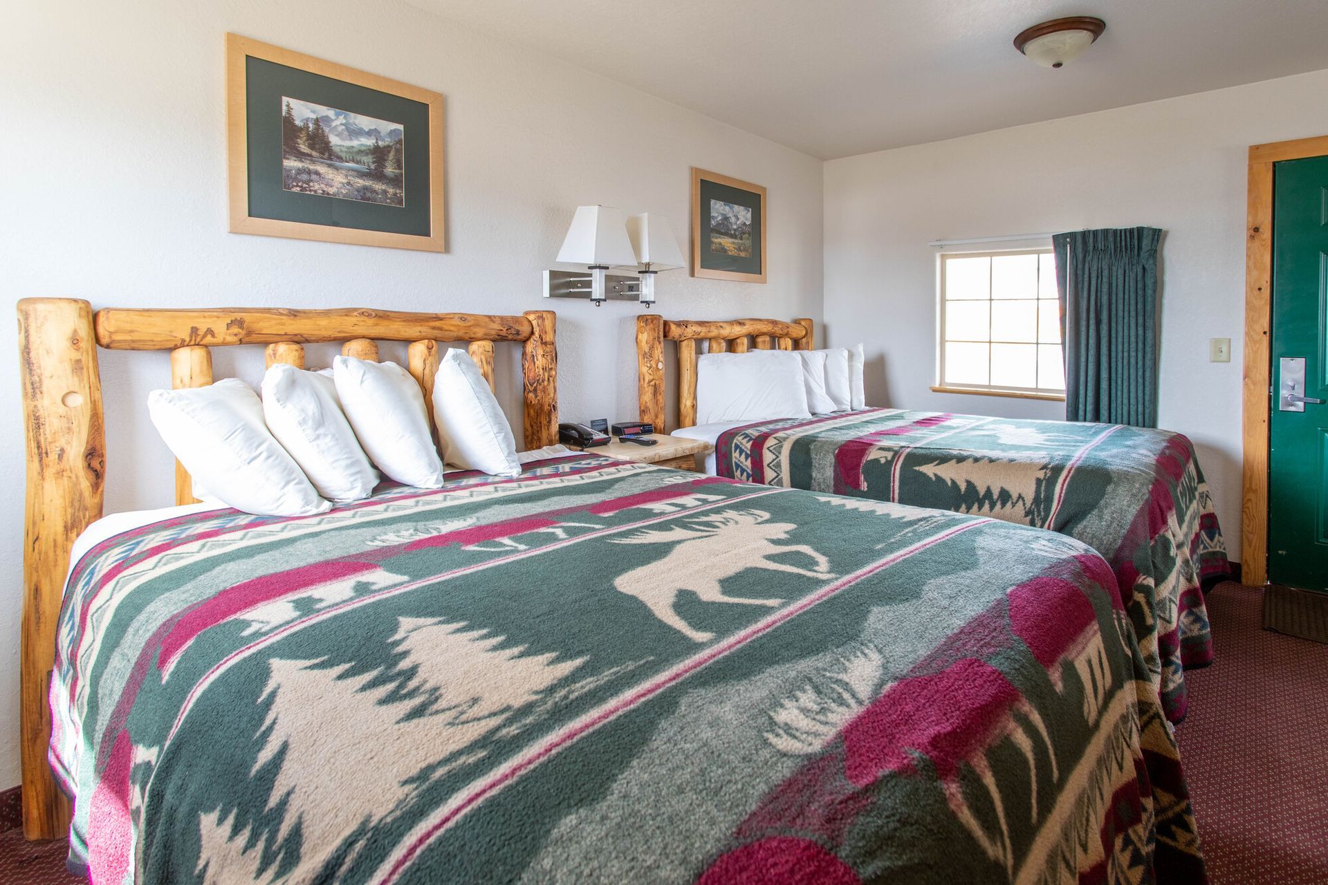 Two double beds with green and red patterned blankets in a motel room.