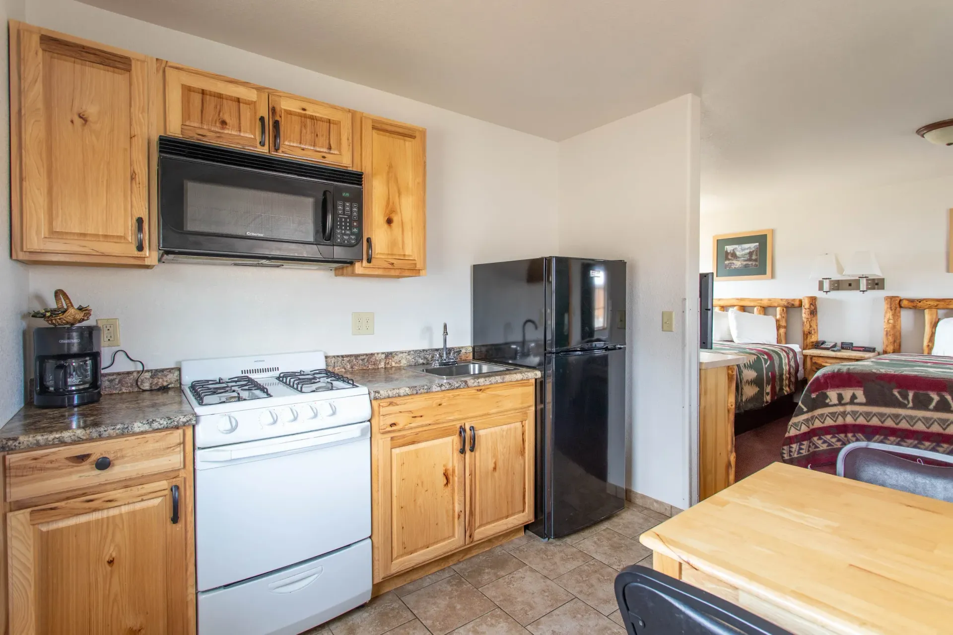 Kitchenette in a cabin with stove, microwave, cabinets, and refrigerator; two beds visible in background.