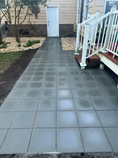 Tiled walkway leading to a white door beside a house, with white stairs and railing on the right.