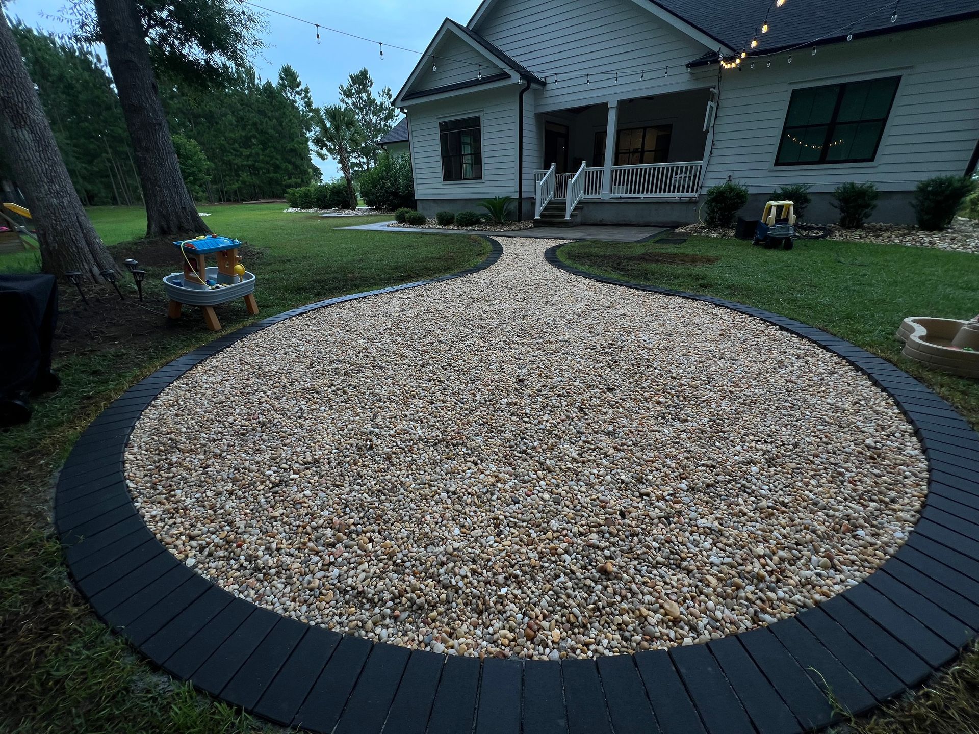 Circular gravel fire pit area with a black border in a front yard beside a white house