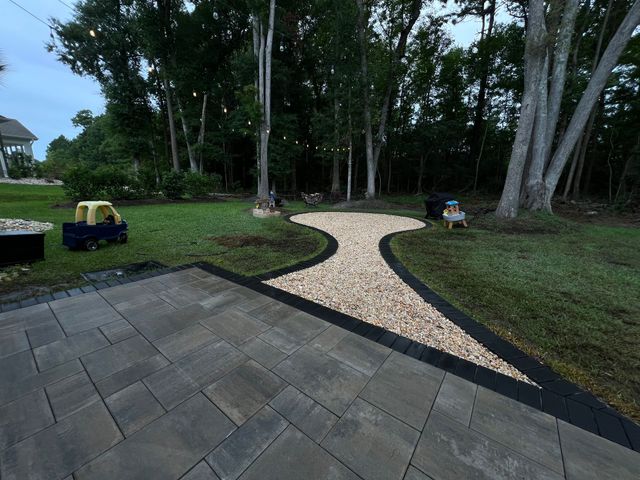 Curved gravel garden path bordered by black edging beside a tiled patio and trees in a park-like yard