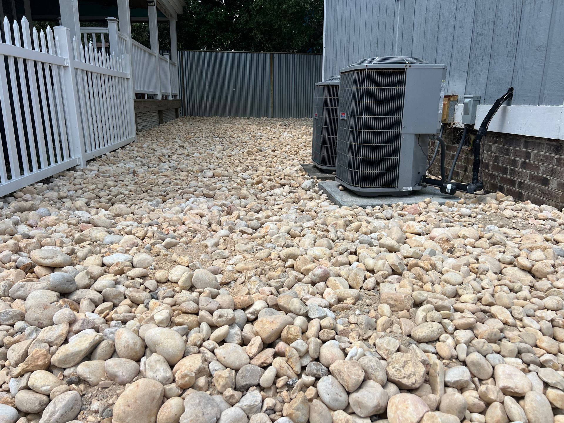 Rock-covered side yard with white fence, gray shed, and outdoor HVAC unit on the right.