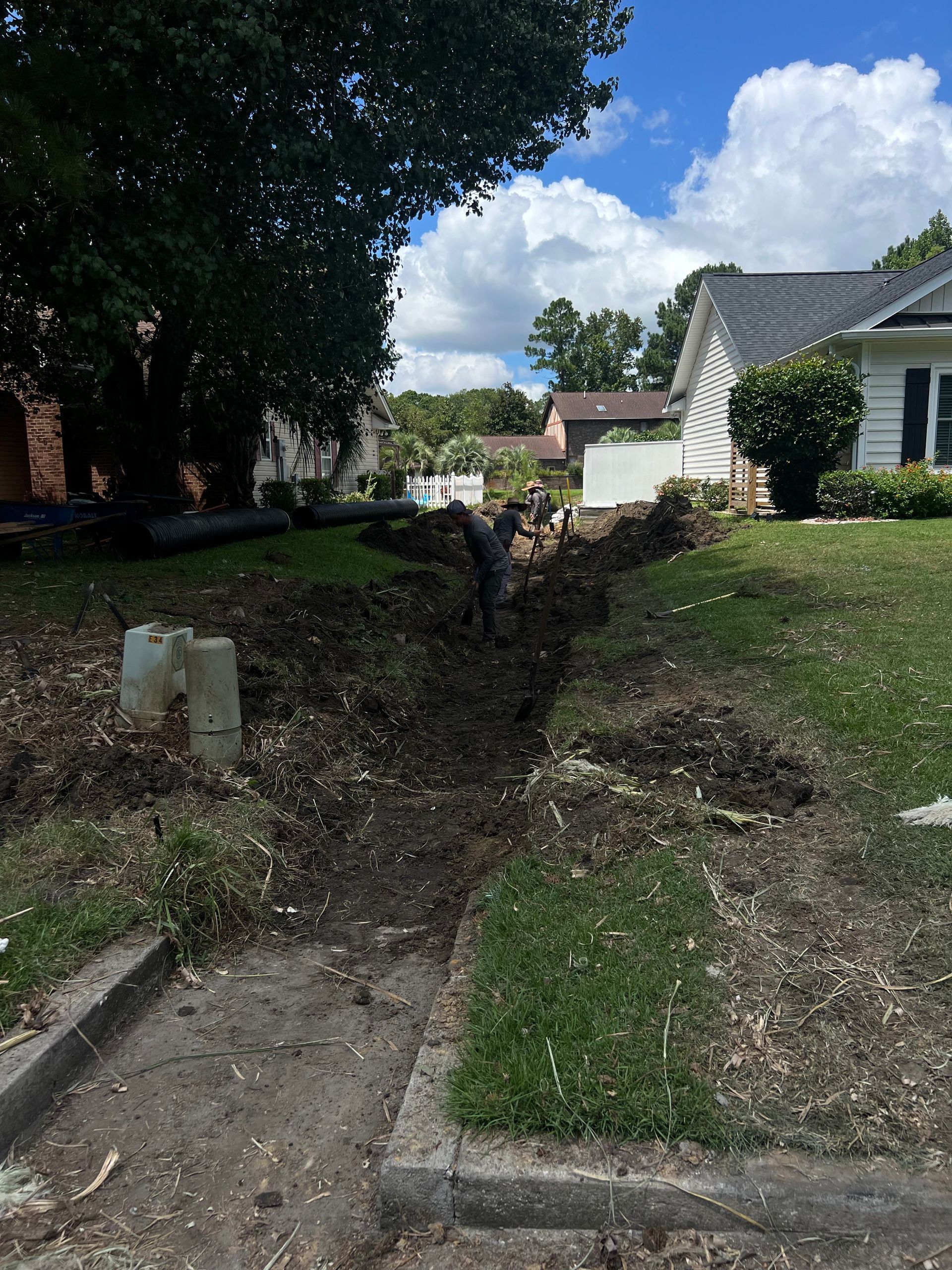 Narrow drainage ditch beside a grassy yard and sidewalk between houses on a sunny day
