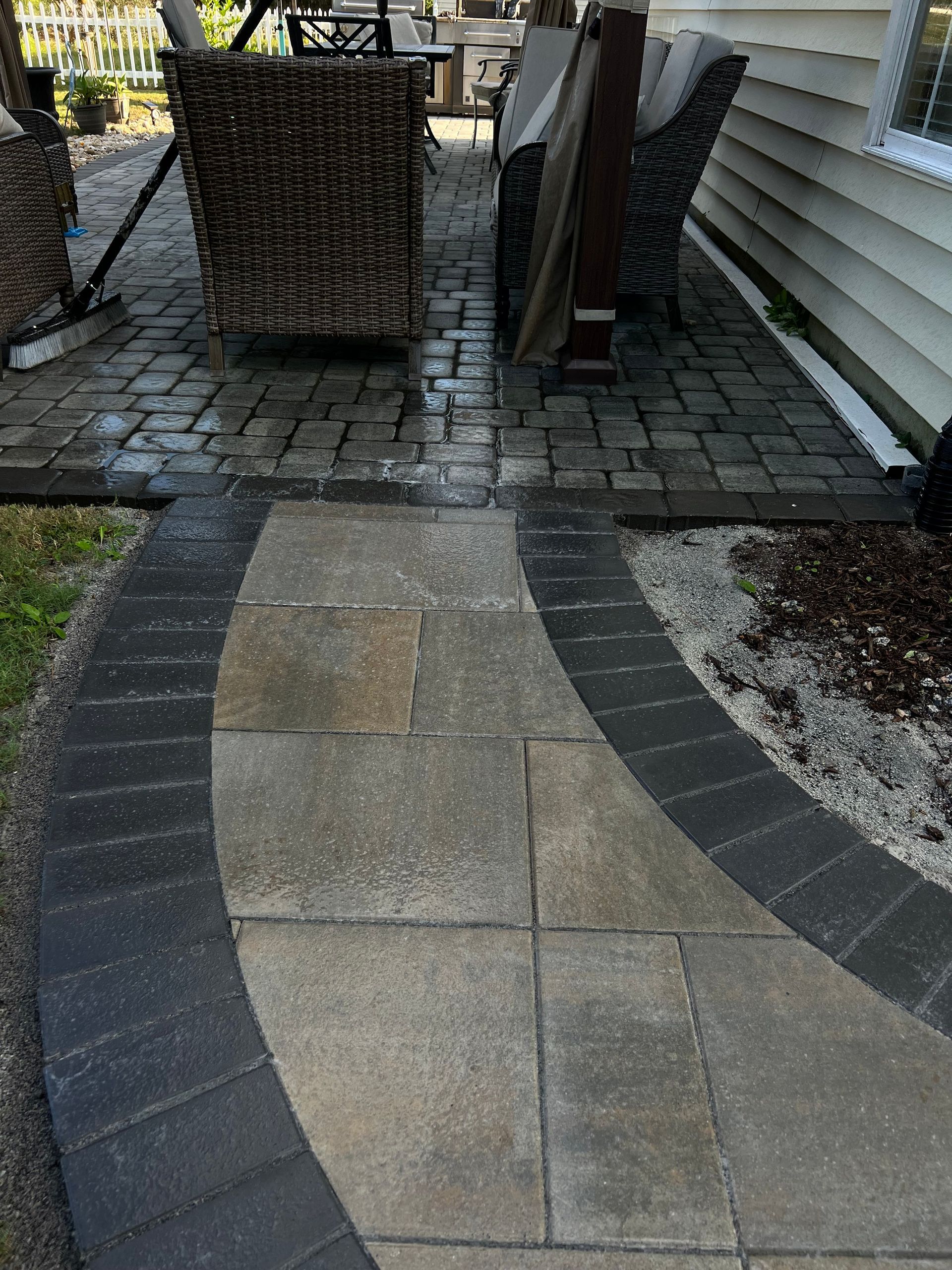 Stone patio walkway leading to outdoor wicker chairs beside a house wall