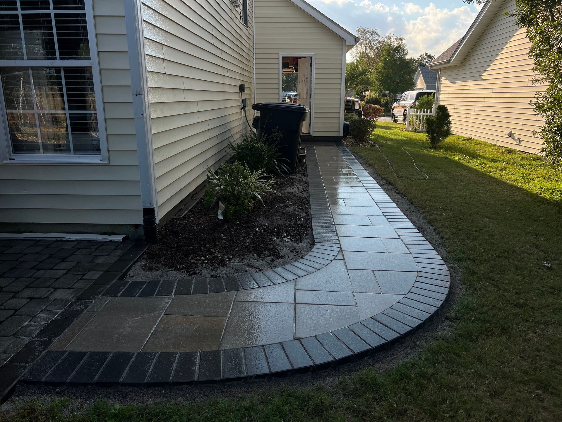Curved paved walkway beside beige houses, with a dark trash bin at the far end.