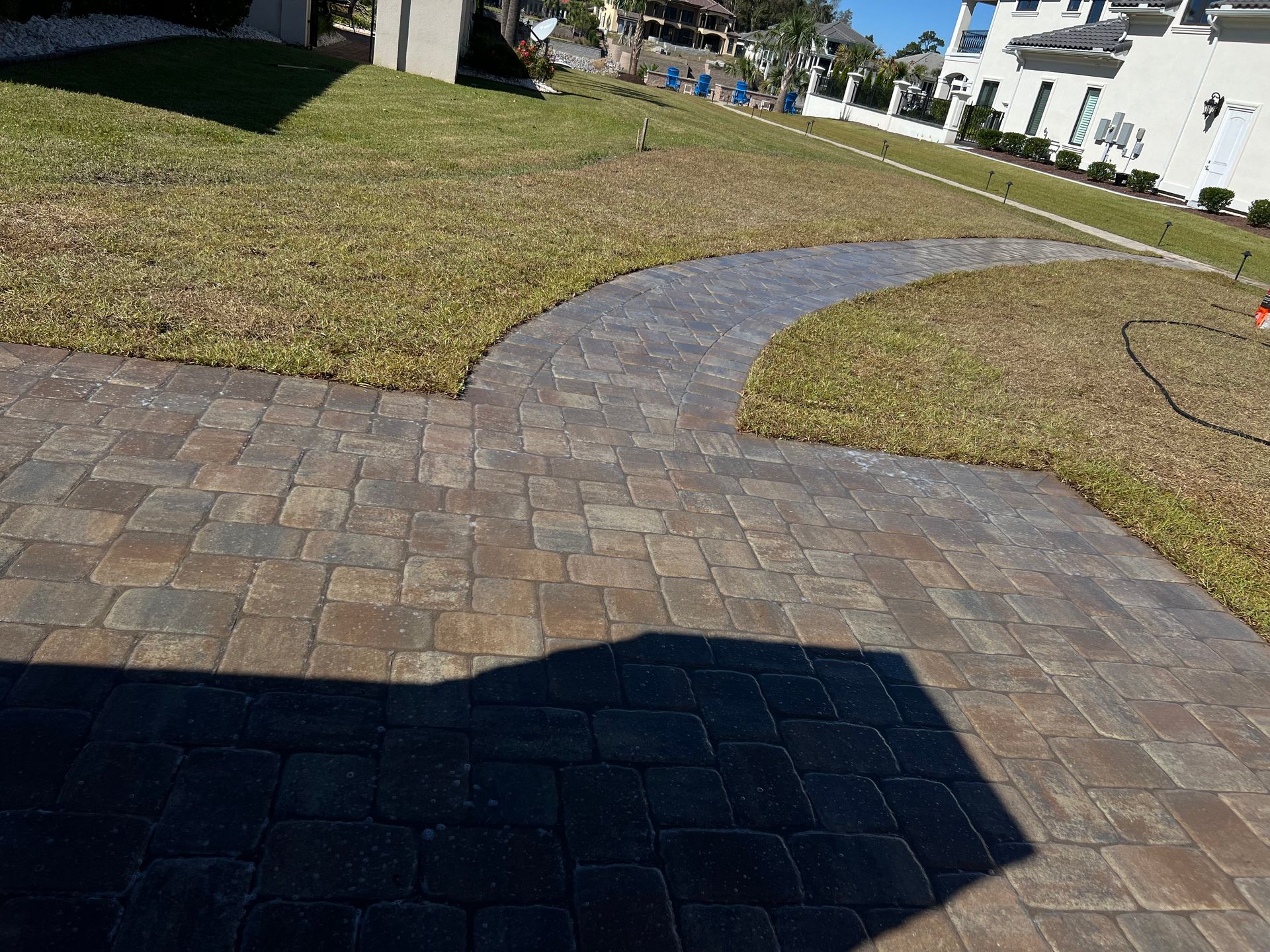 Curved stone walkway through a grassy courtyard with buildings in the background and a shadow in front