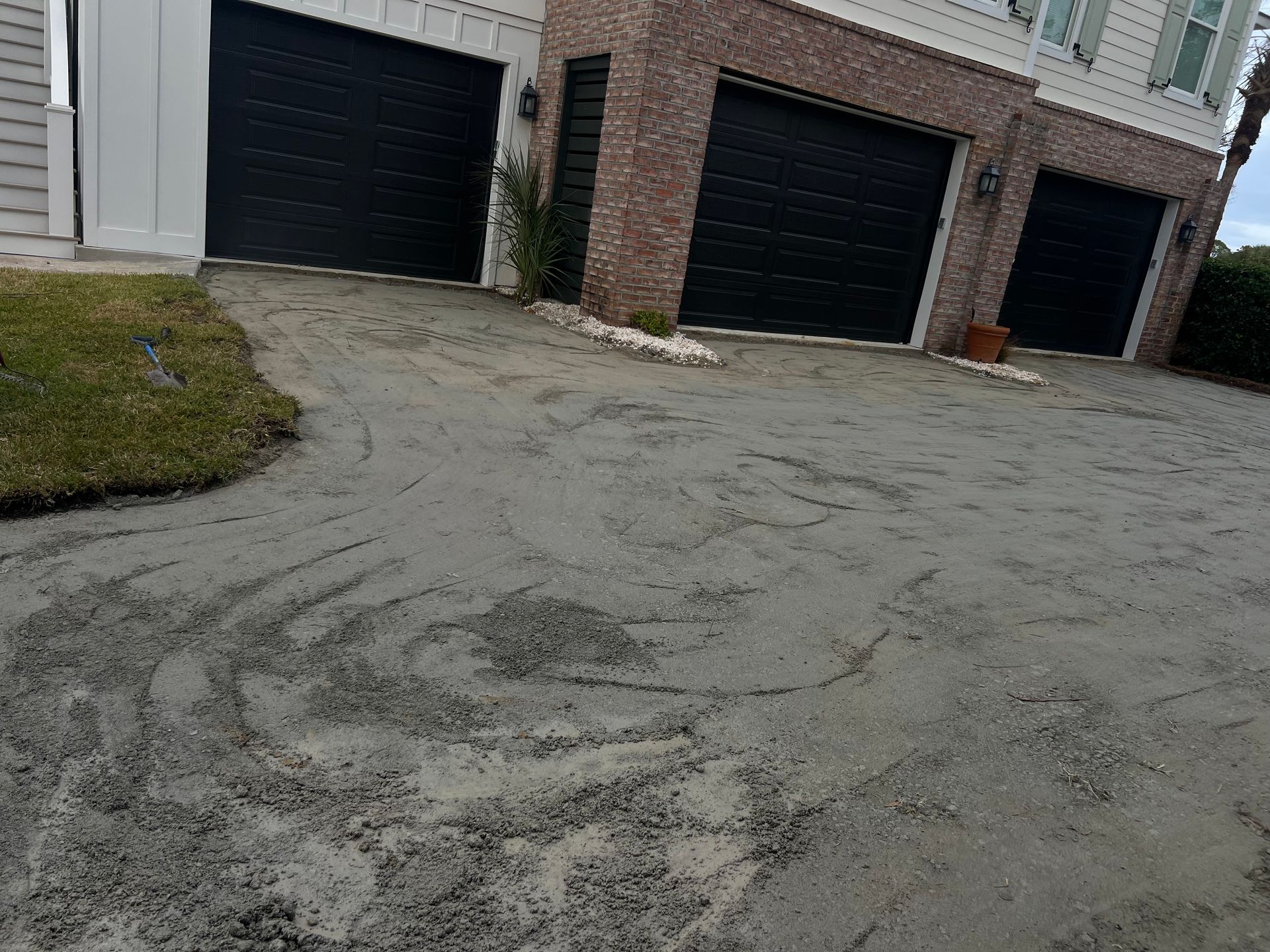 A cracked asphalt driveway lined with black garage doors and a small patch of grass.