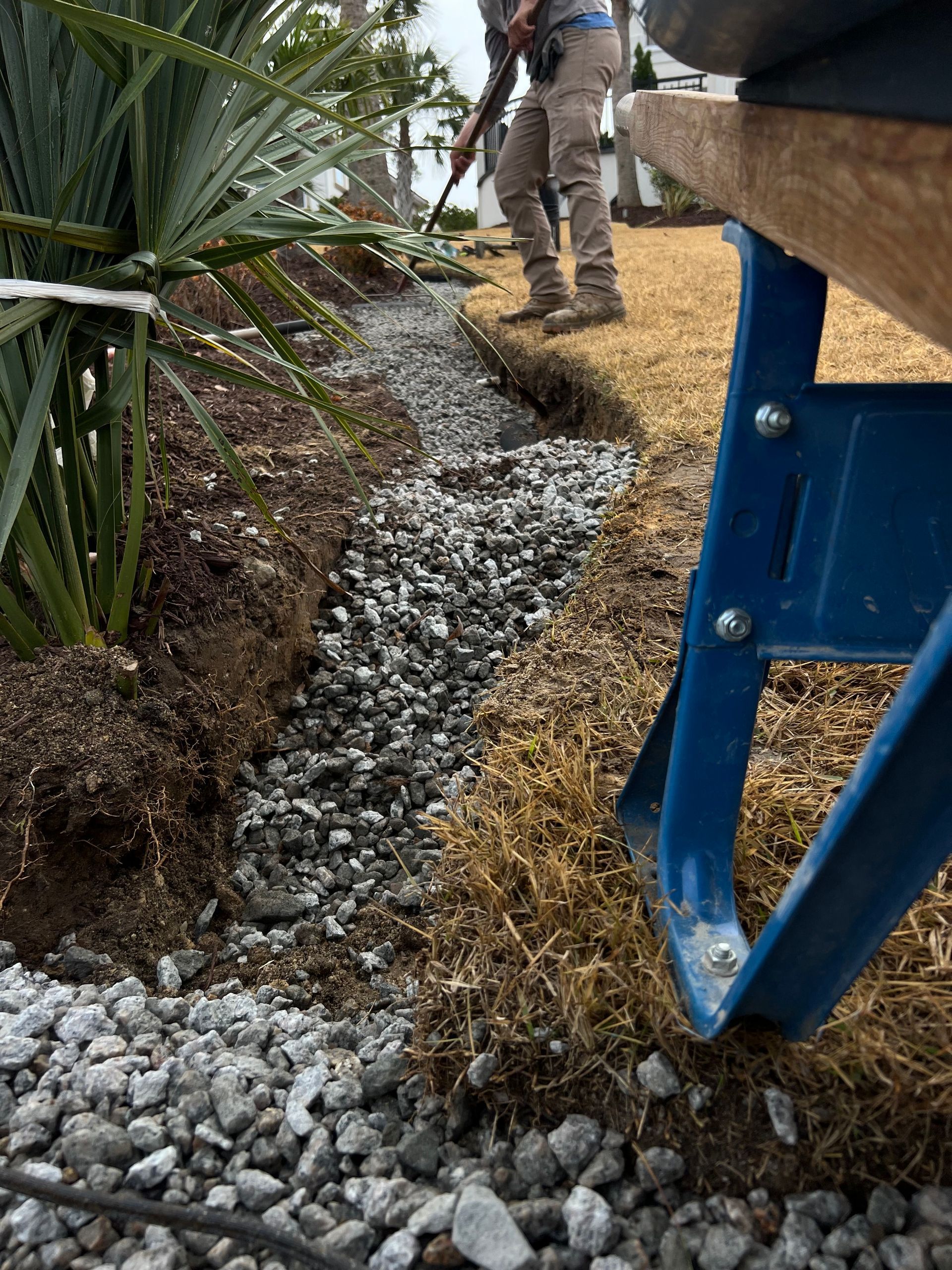 Worker spreading gravel in a landscaped trench beside blue equipment outdoors