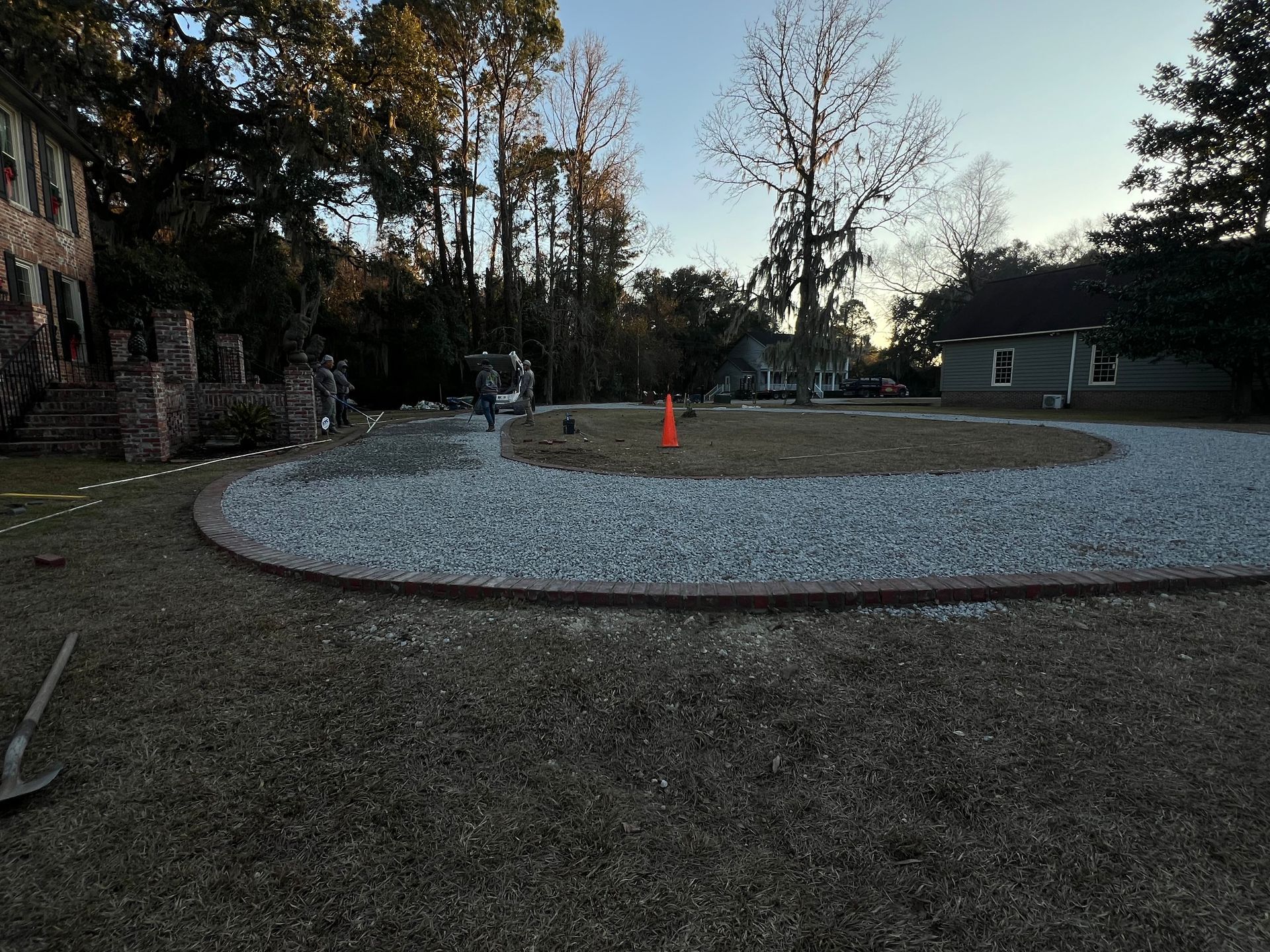Gravel driveway turnaround with orange cone, surrounded by trees at dusk