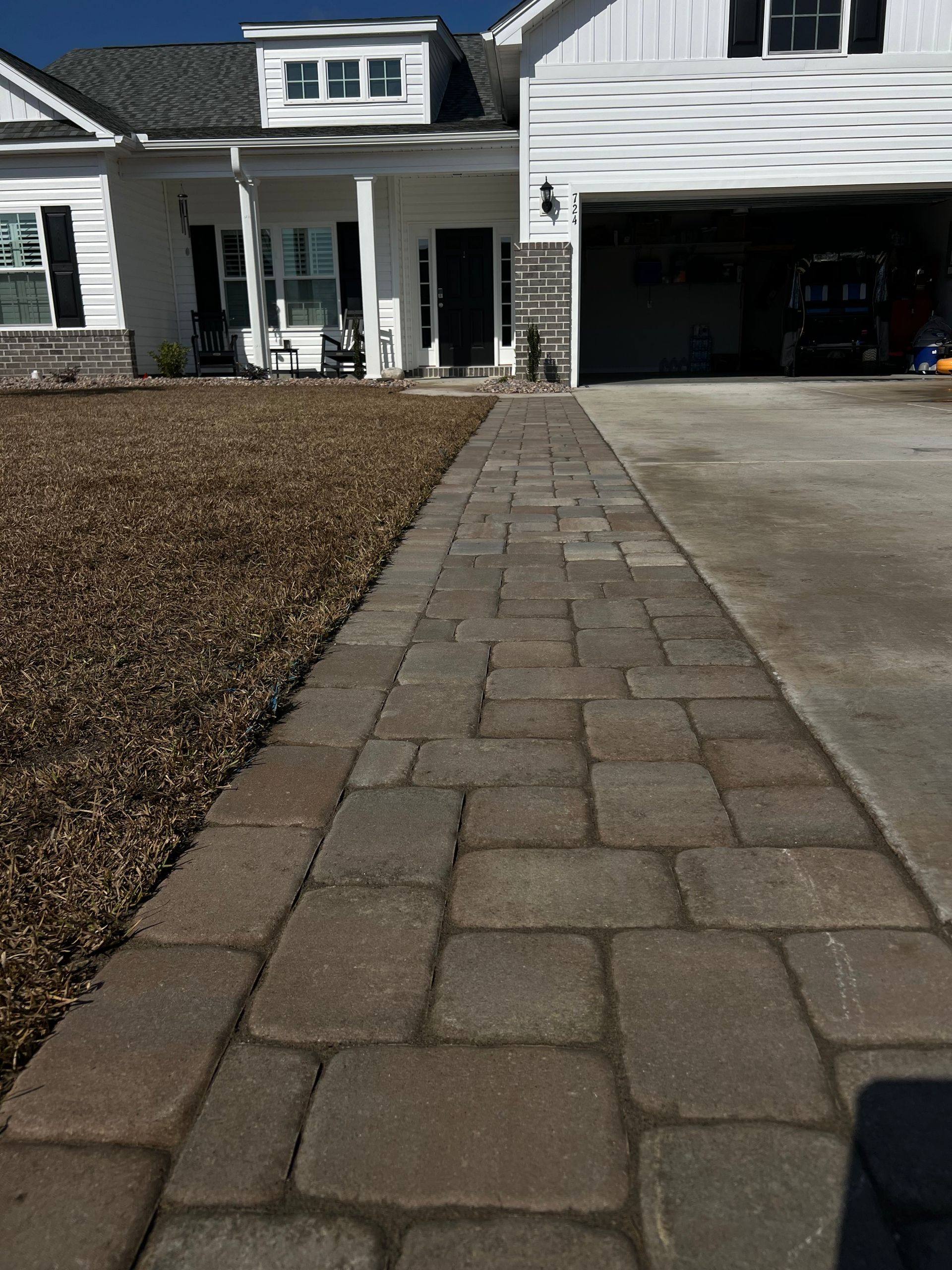 Paver walkway leading to a white house with garage and front entrance on a sunny day