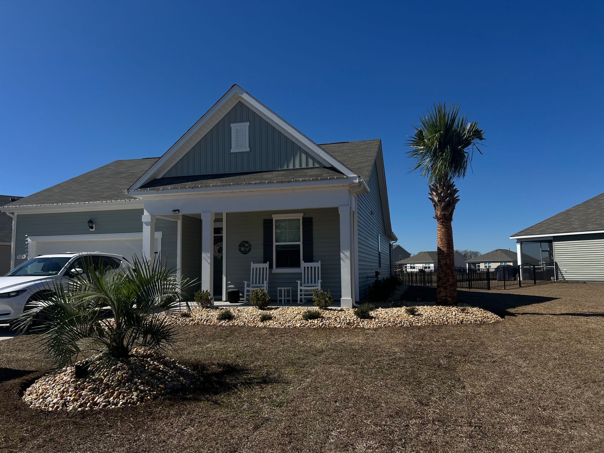 White farmhouse with porch, gravel yard, and palm tree under a clear blue sky