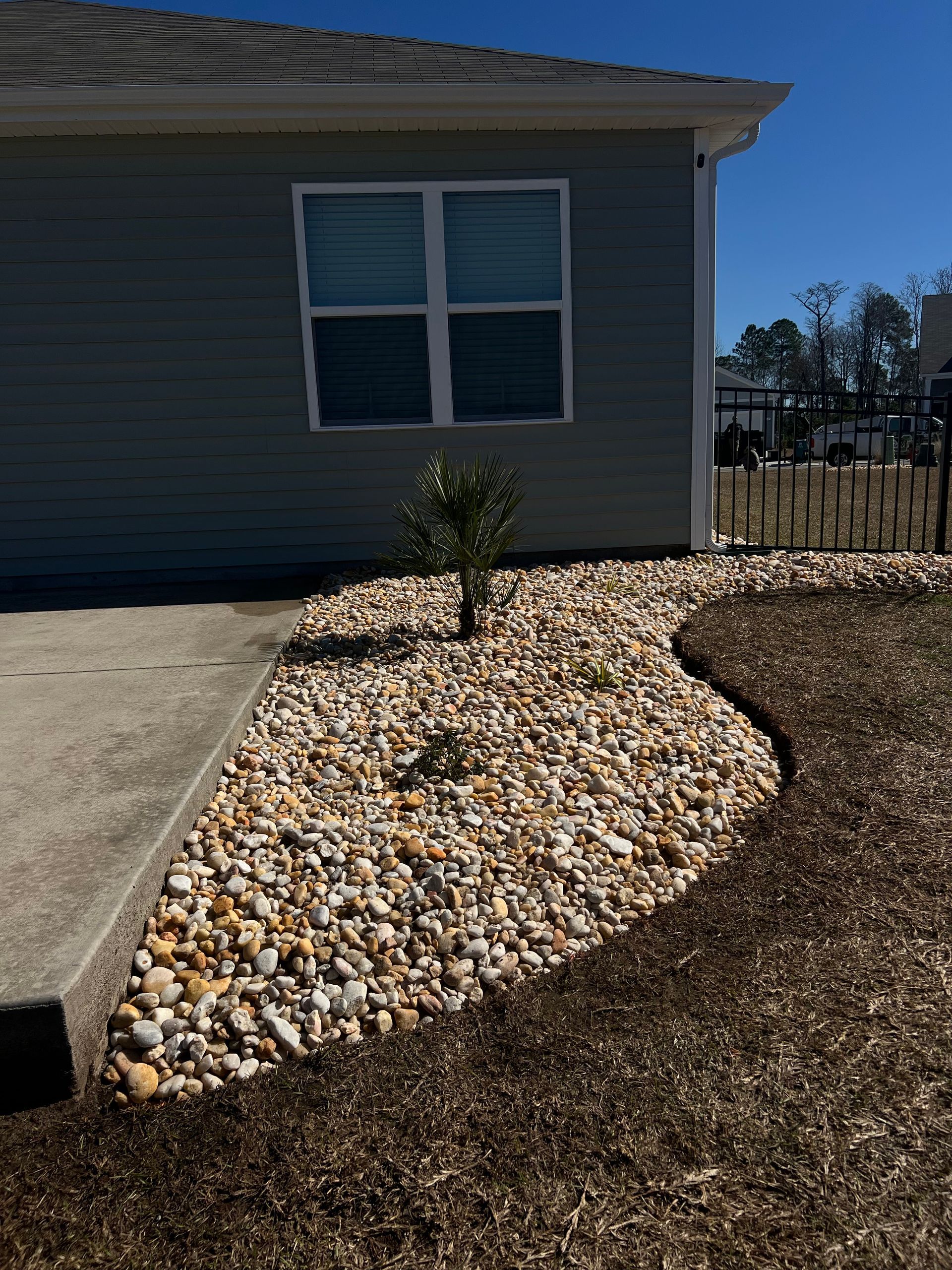 House exterior with a front window, concrete walkway, and a rock landscaping bed with a small shrub.
