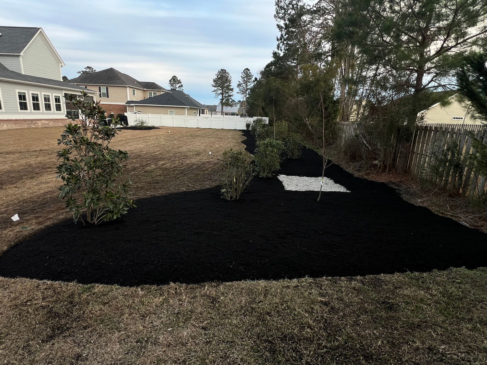 Fresh black mulch covering a landscaped backyard bed beside houses and trees