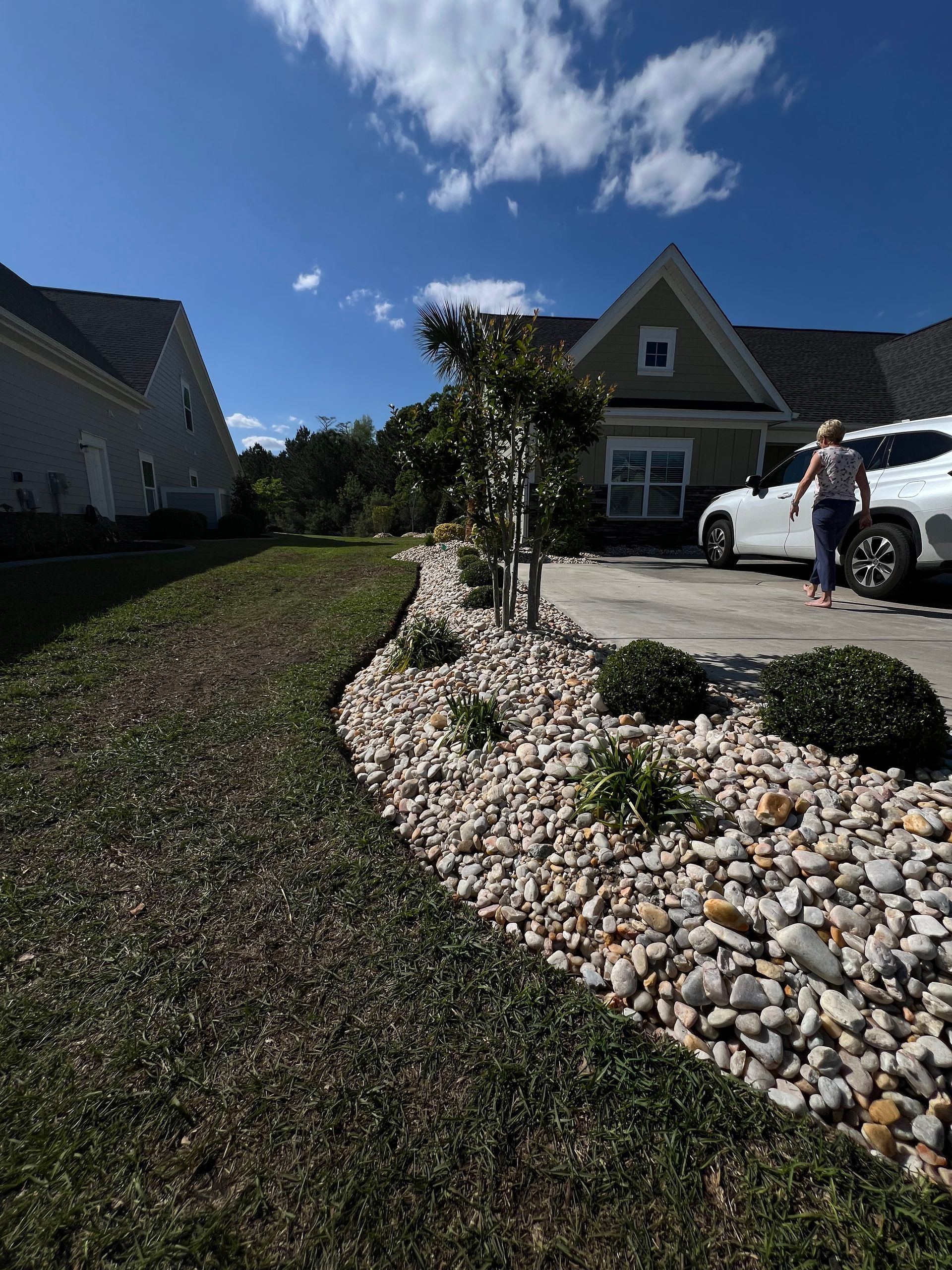 Suburban house with landscaped rock bed and a person standing beside a white truck in the driveway