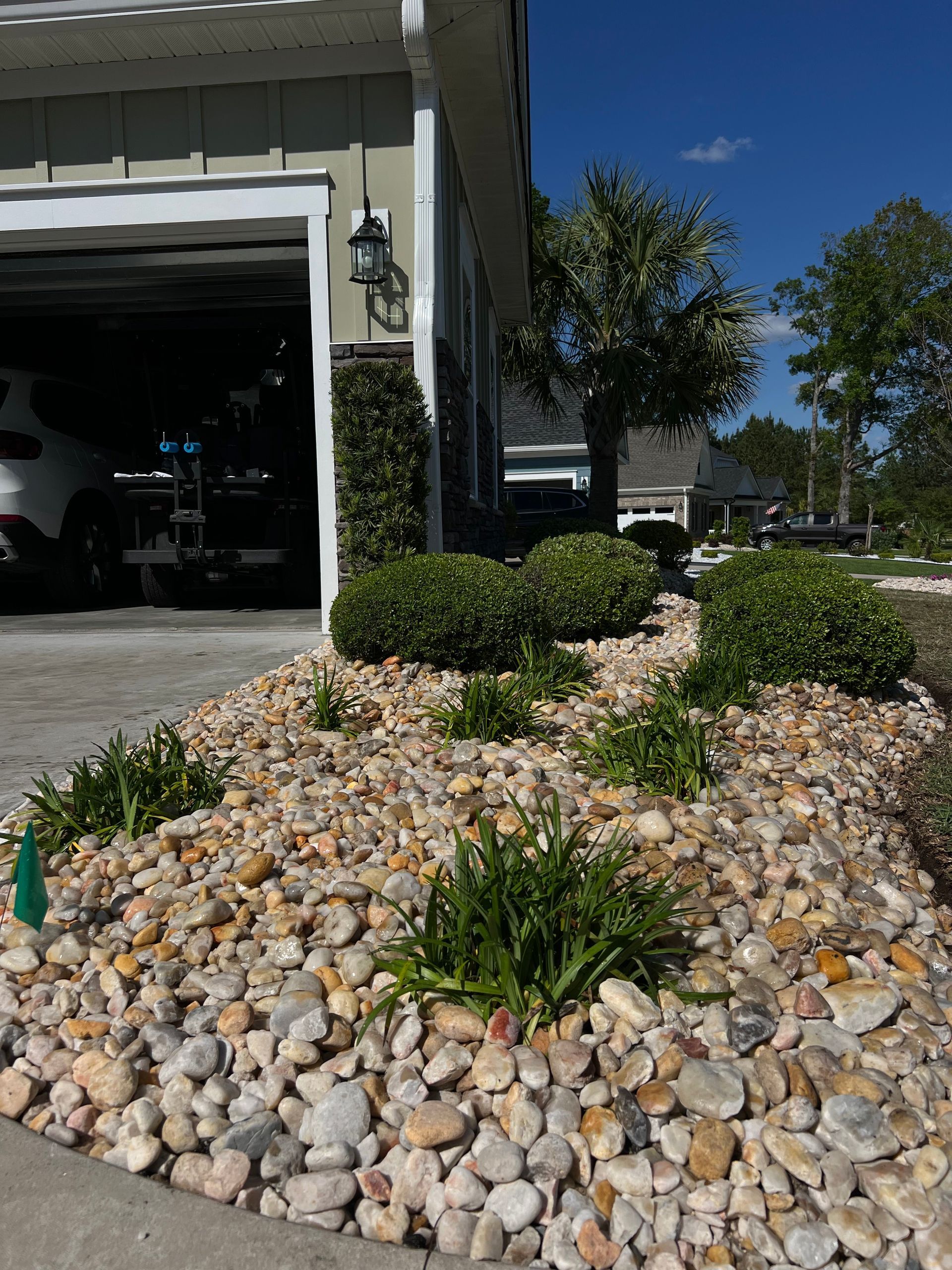 Front yard rock garden with shrubs beside an open garage and house exterior
