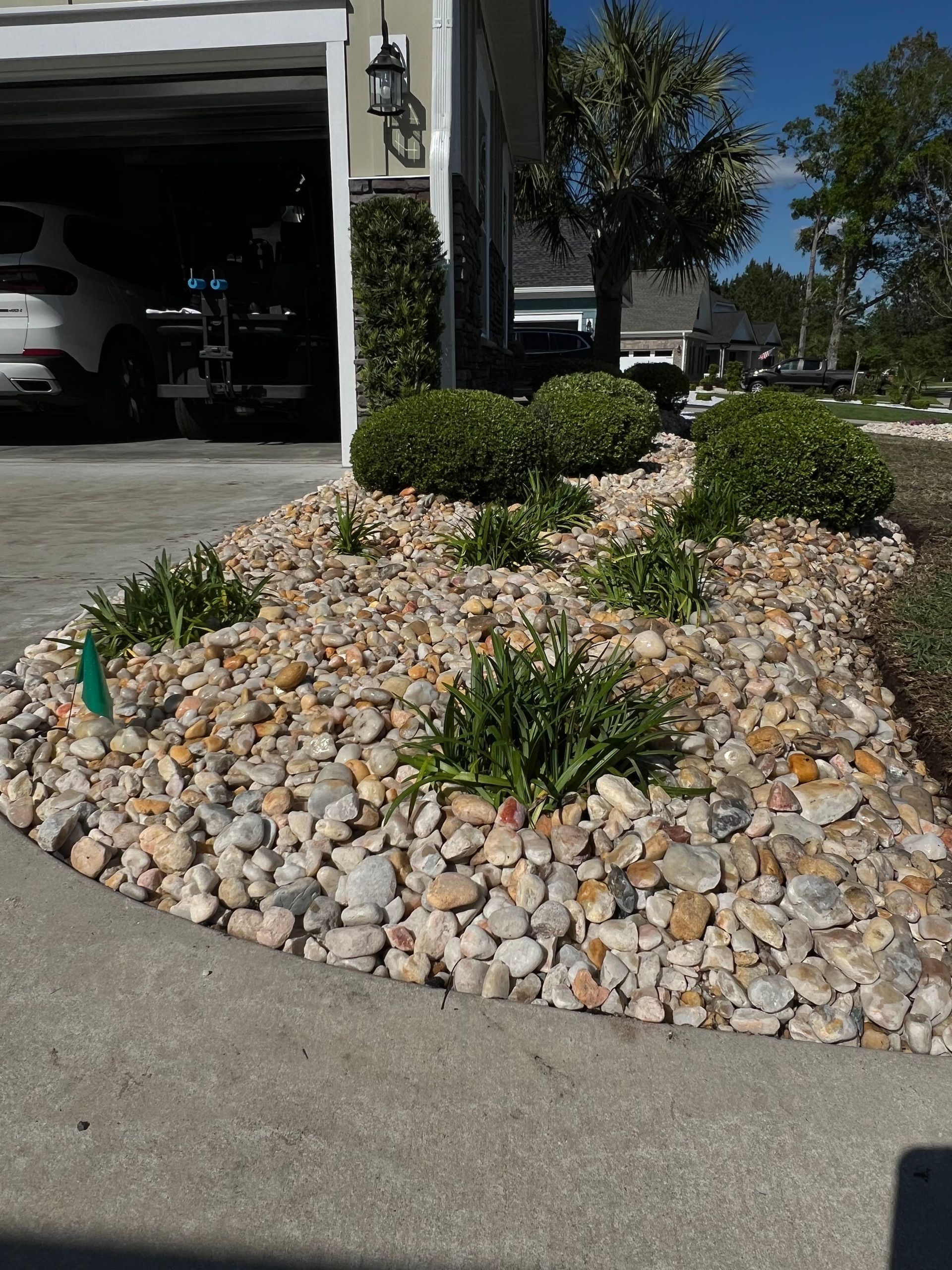 Front yard rock garden with shrubs beside a driveway and open garage on a sunny day