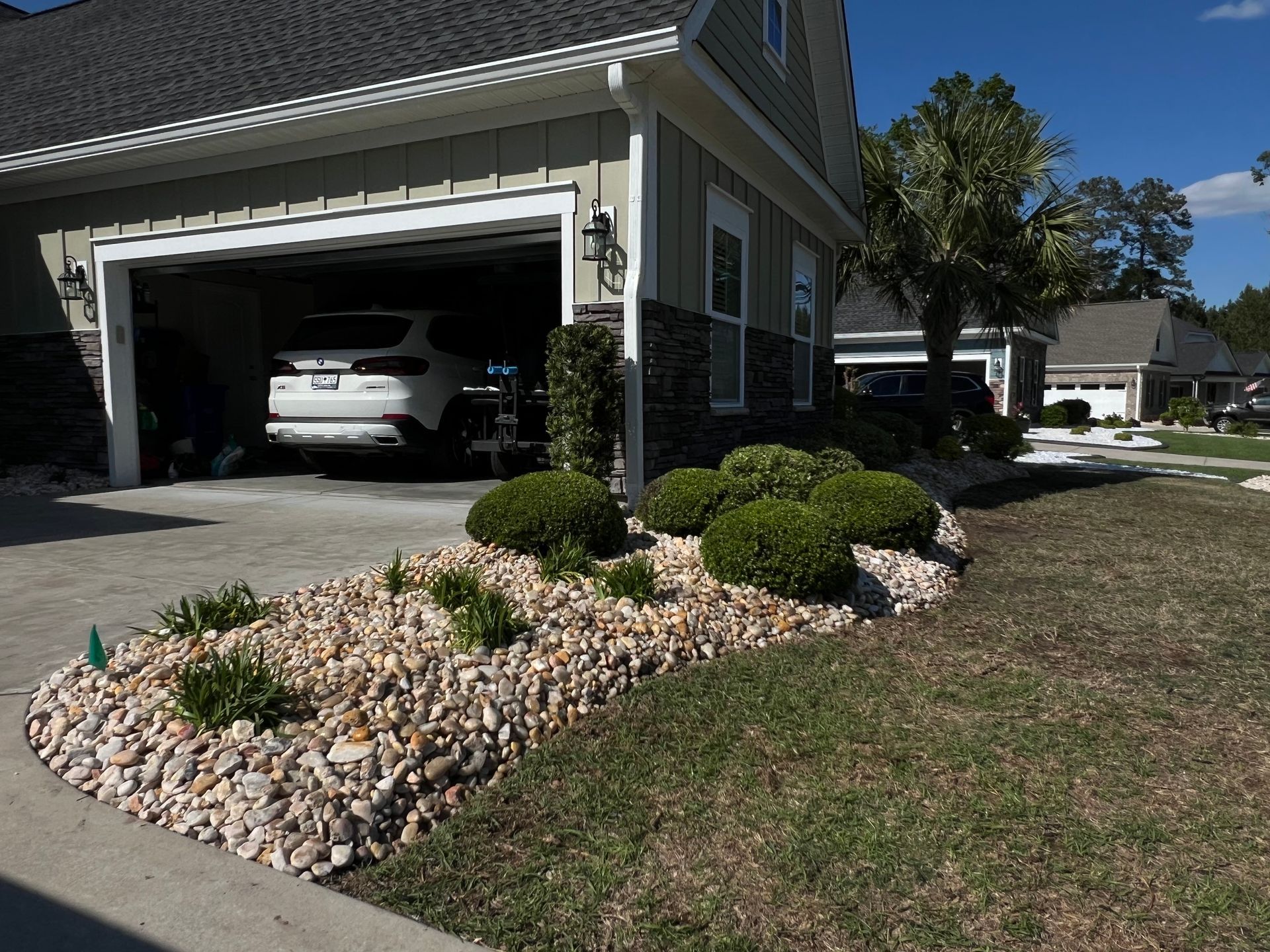 Suburban house with open garage, white car, and landscaped front yard with rock beds