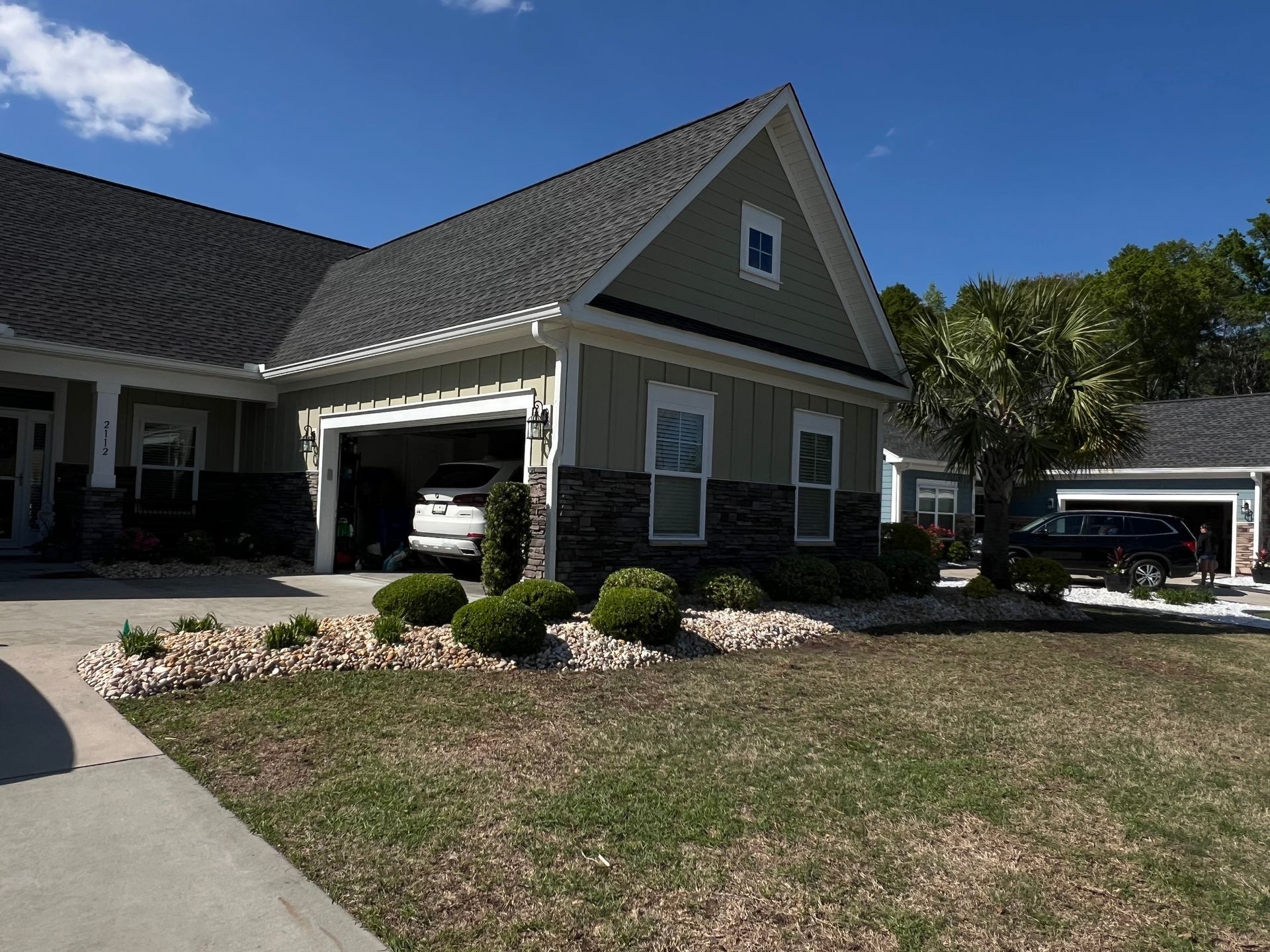 Suburban house with a covered porch, attached garage, and a dry front lawn under a blue sky