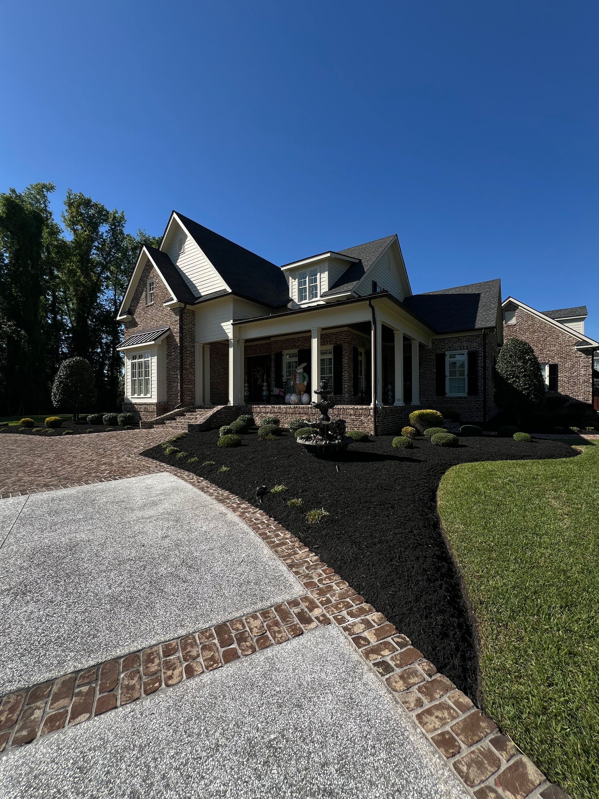 Suburban brick house with steep roof, front porch, and gravel driveway under a clear blue sky
