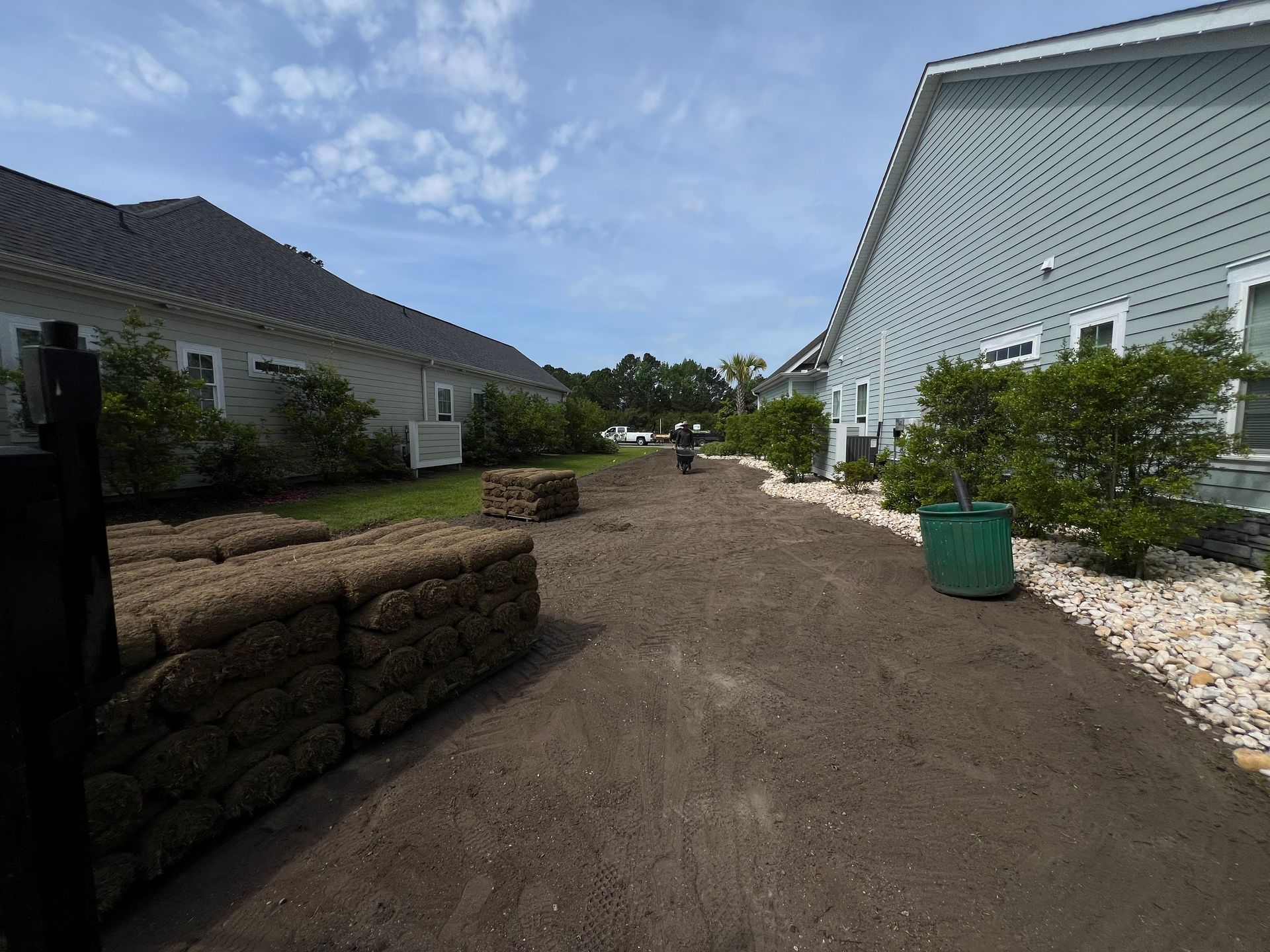 Residential walkway between white houses with landscaped bushes and rock borders on a sunny day