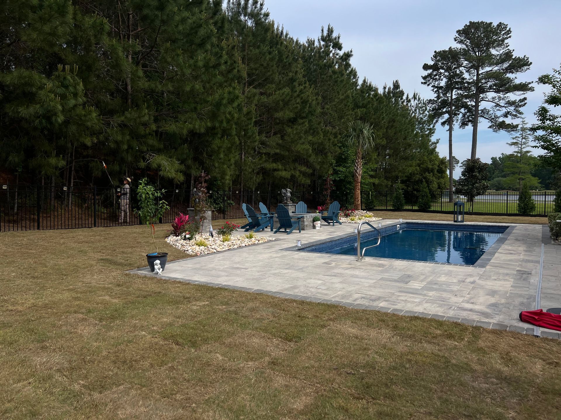 Backyard pool beside a grassy lawn, with trees, lounge chairs, and a flower bed along the deck