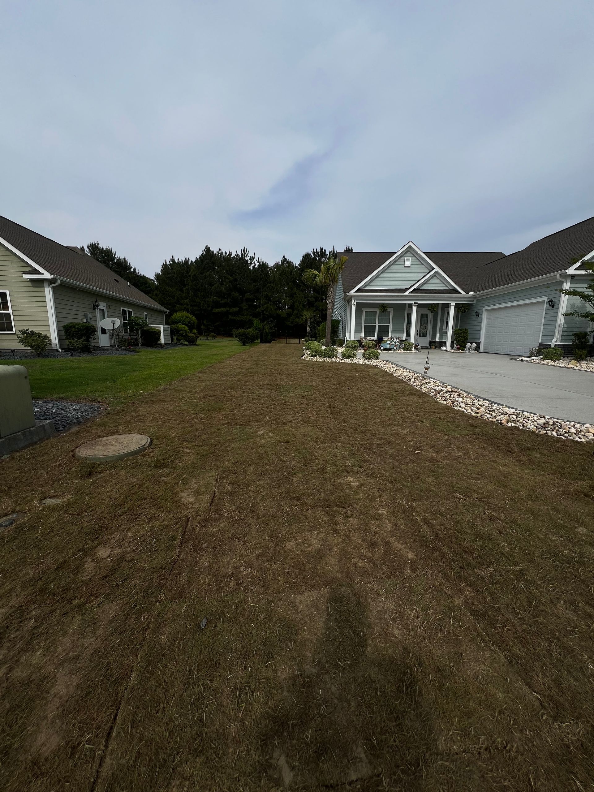 Mud-filled front yard between two houses, with a driveway and covered porch in the background.