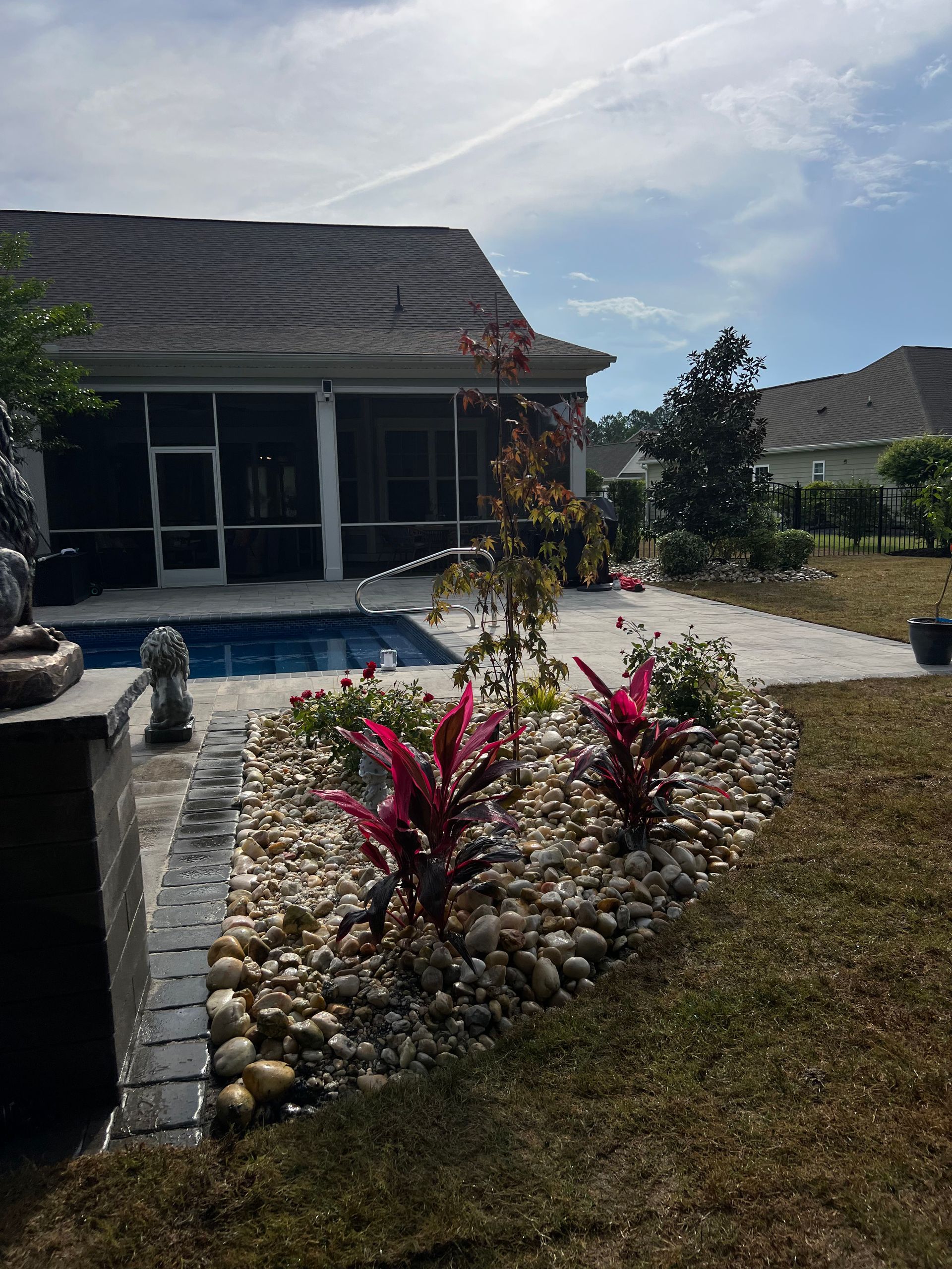 Backyard patio with a pool, stone garden bed, and small flowering shrubs beside a house