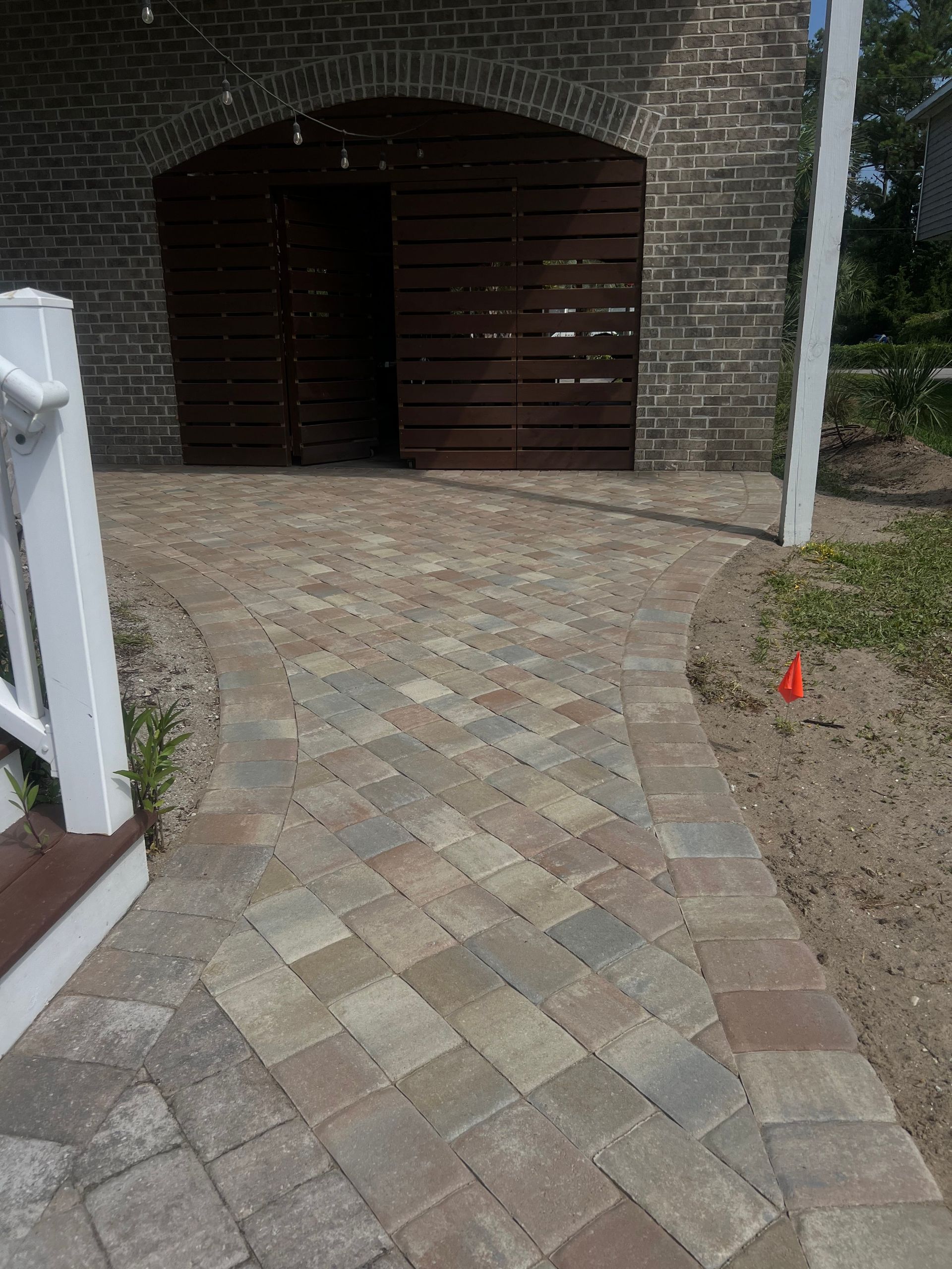 Brick driveway leading to a double wooden garage door under an arched brick entrance