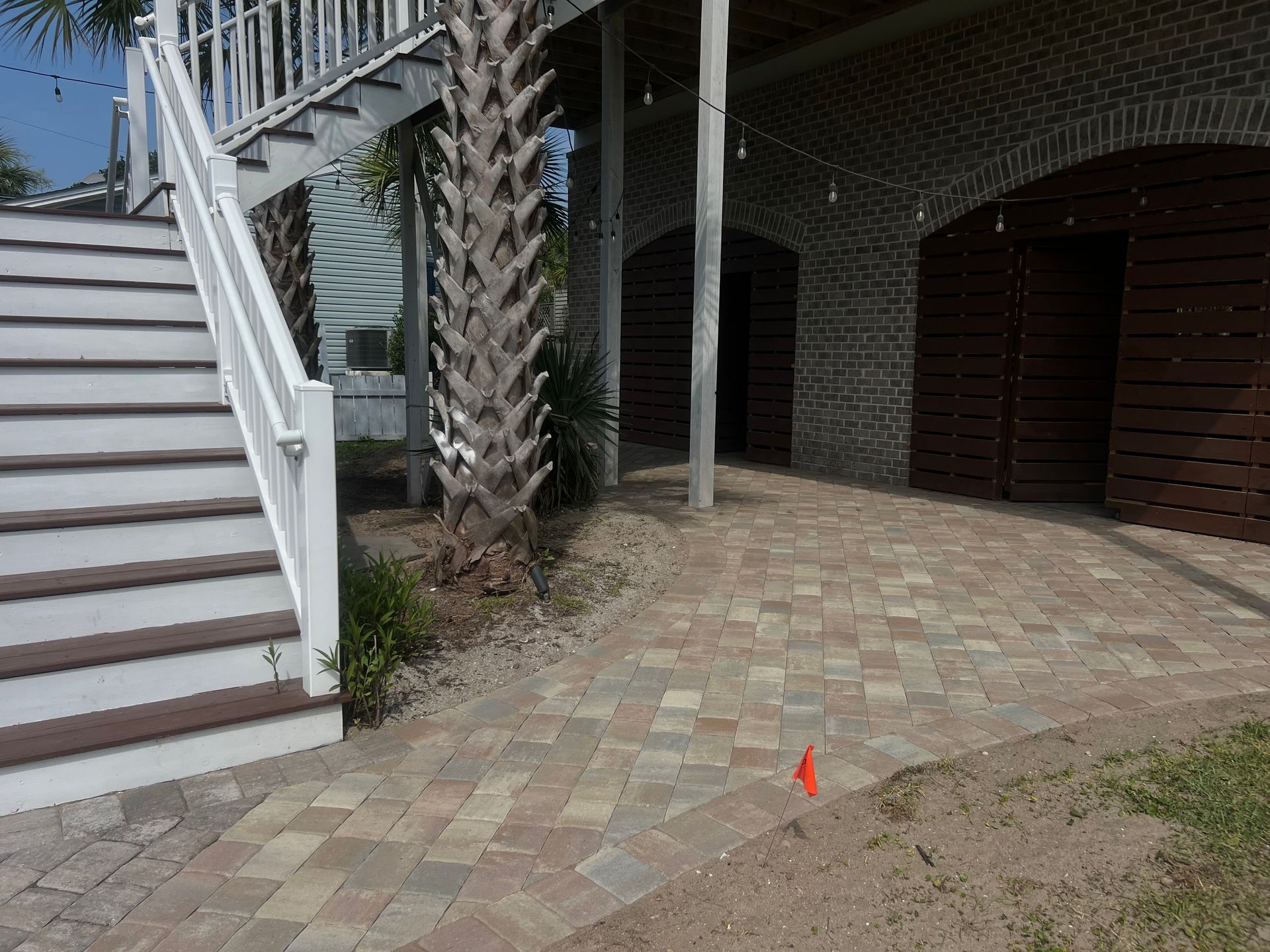 Front porch with white stairs, palm tree, brick pavers, and brown doors beside a house entryway