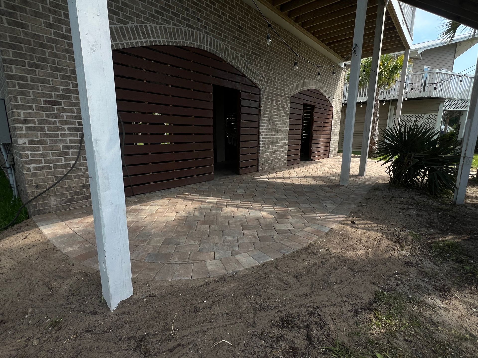 Covered brick walkway with white columns and dark wooden doors beside a paved path