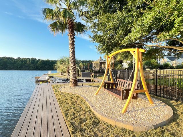 Lakeside boardwalk with a yellow swing bench under trees on a sunny day