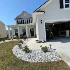 Suburban house with white siding, garage, driveway, and a landscaped front yard under a blue sky
