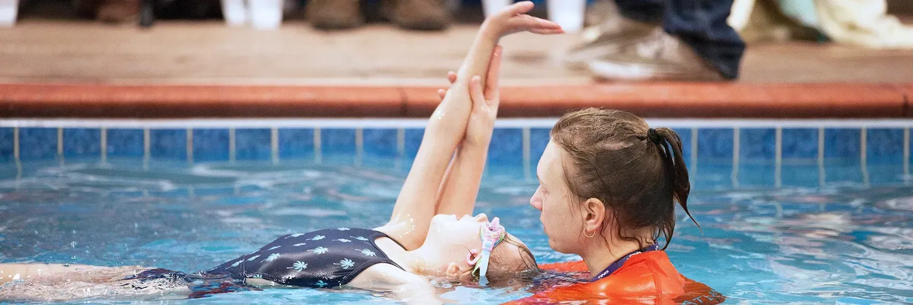 A person in a swimsuit practices synchronized swimming with the assistance of a coach in a pool.
