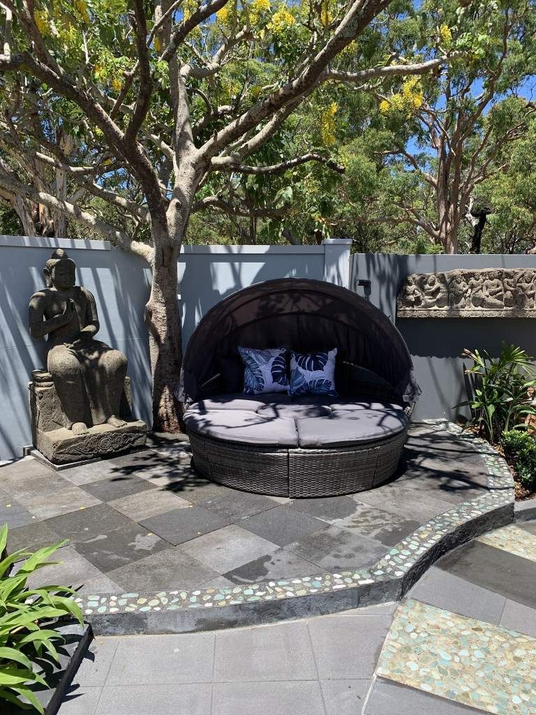 A Wicker Day Bed is Sitting Under a Tree in a Garden — Bali at the Bay in Nelson Bay, NSW