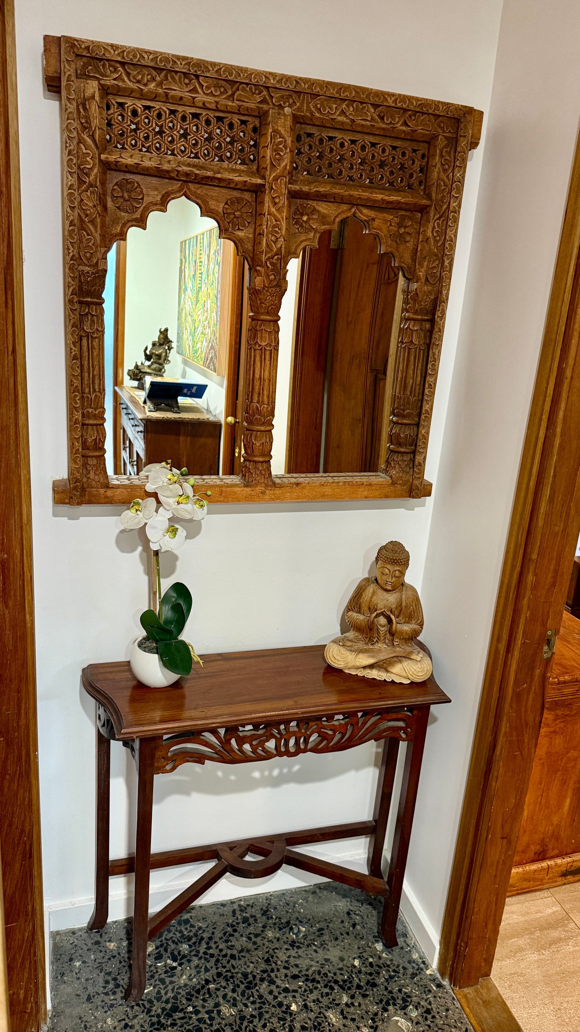 Wooden carved mirror above a table, a Buddha statue, and a potted orchid — Bali at the Bay in Nelson Bay, NSW