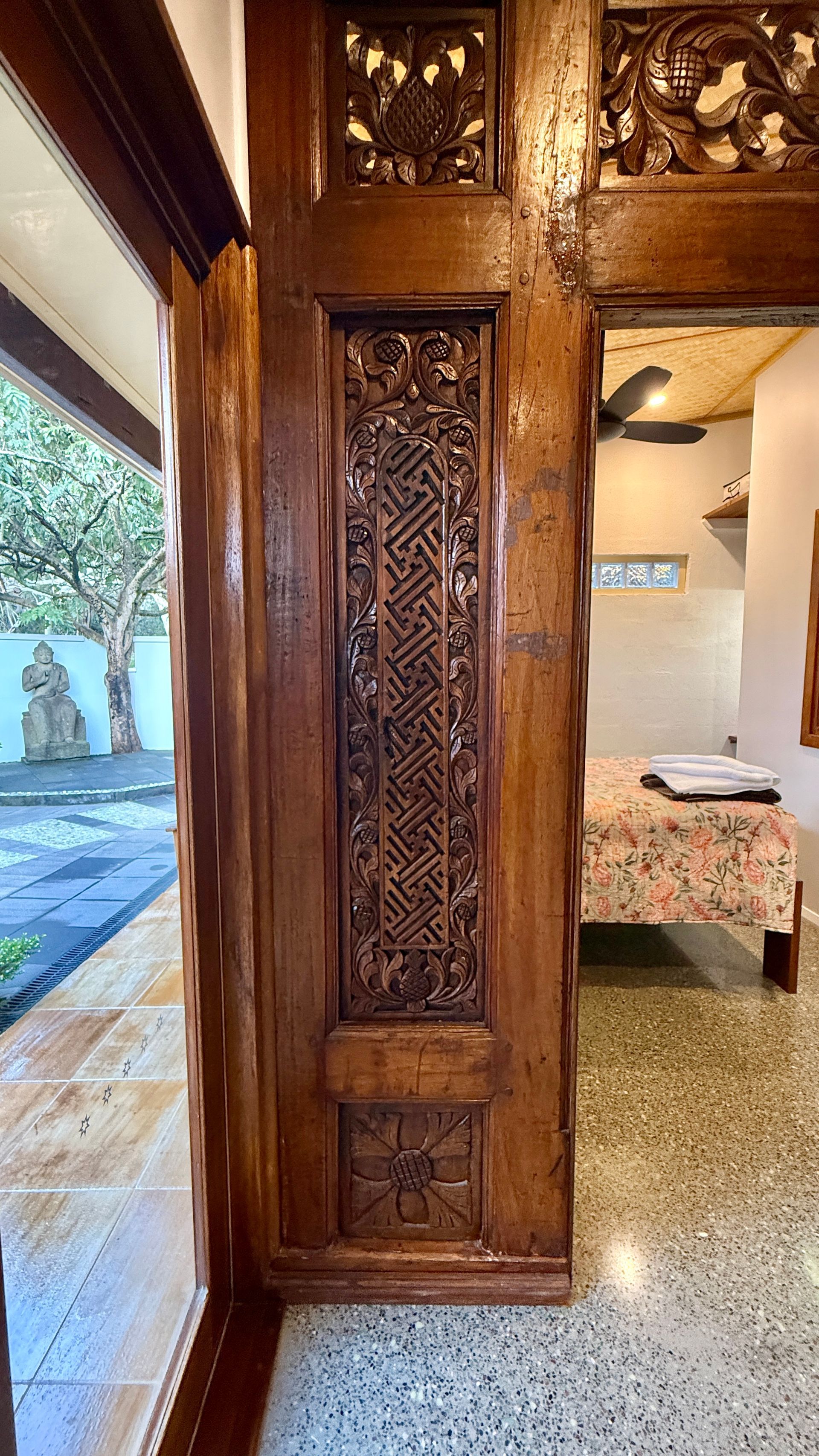 Ornate wood doorway with carved panels; view into a bedroom with a floral bedspread — Bali at the Bay in Nelson Bay, NSW