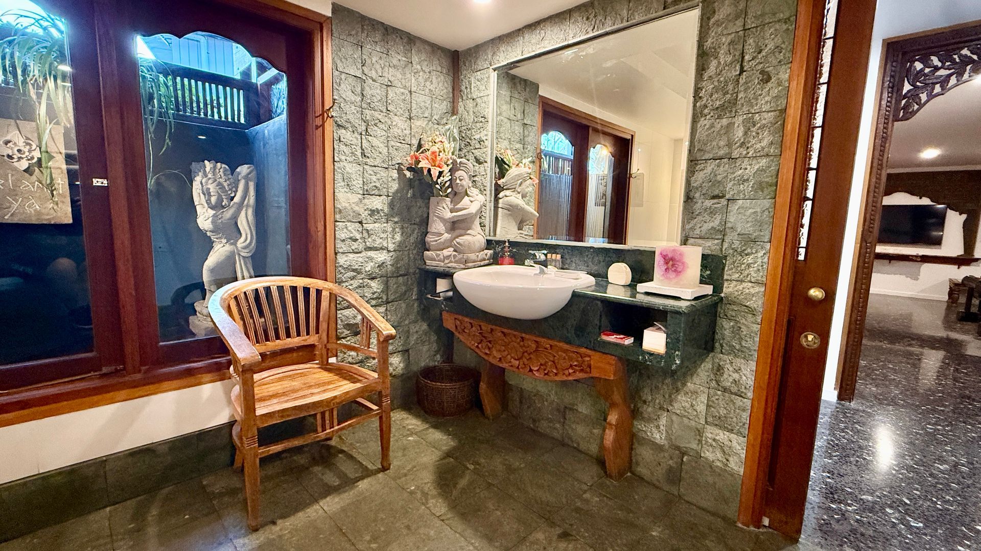 Bathroom with stone walls, wooden chair, sink, mirror, and outdoor view — Bali at the Bay in Nelson Bay, NSW