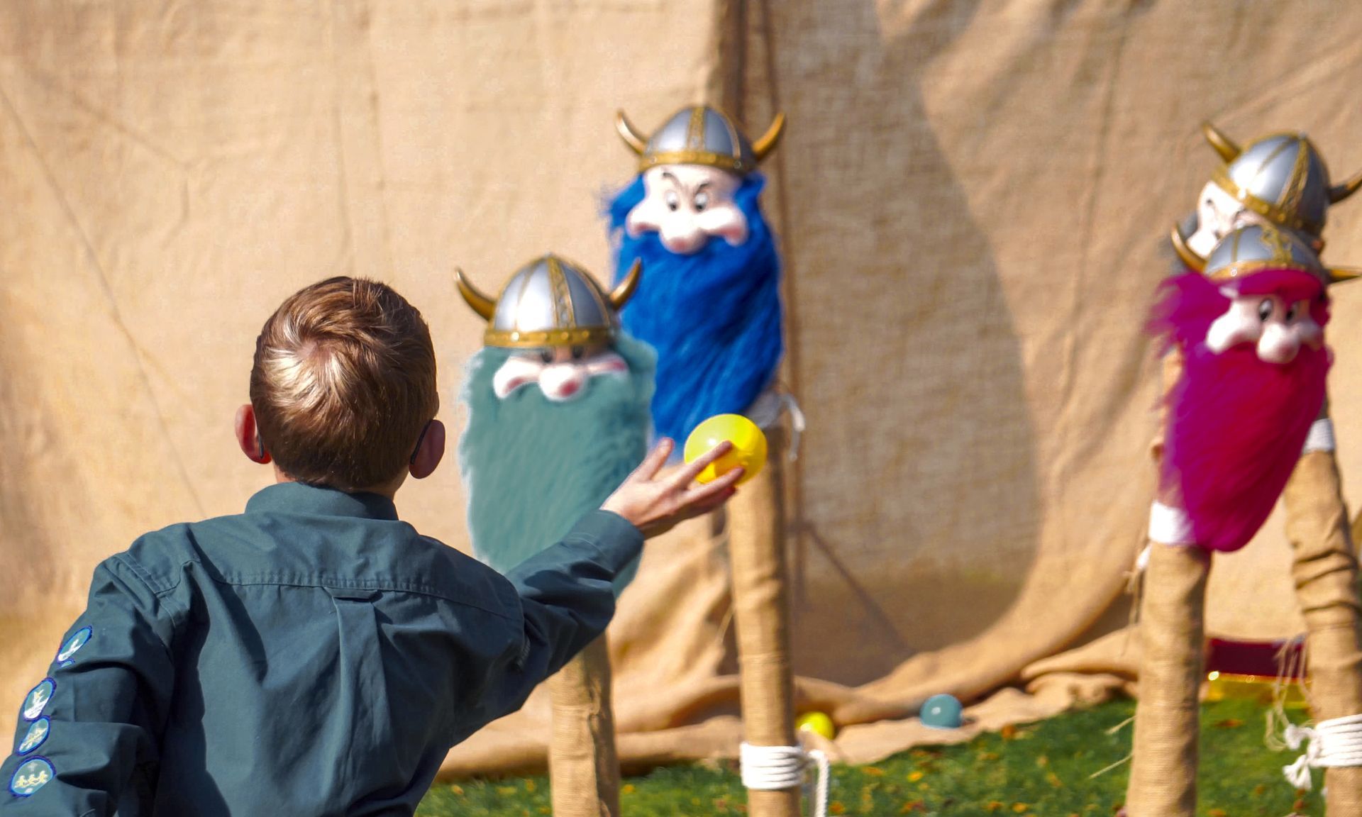 A boy is throwing a ball at a target with viking helmets on it.
