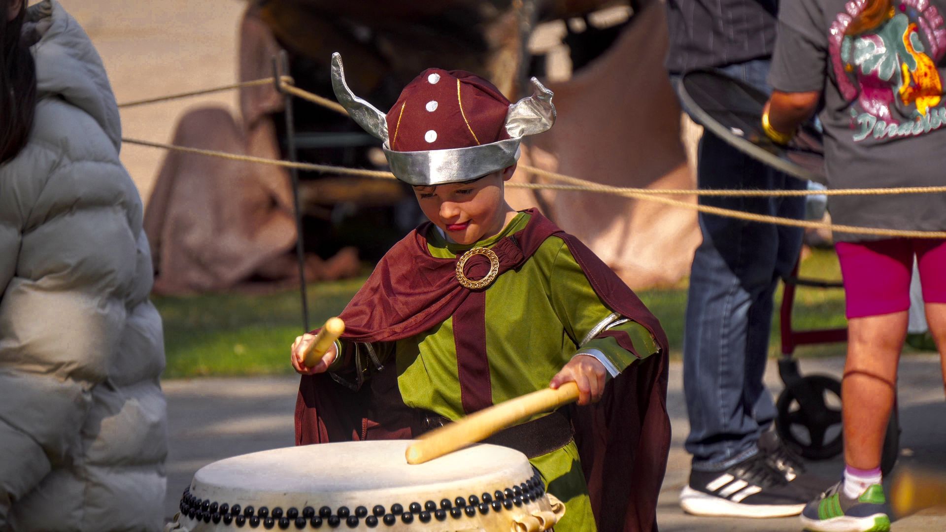 A young boy dressed as a viking is playing a drum.