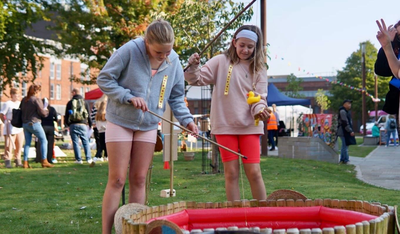 Two young girls are playing a game of fishing in a park.