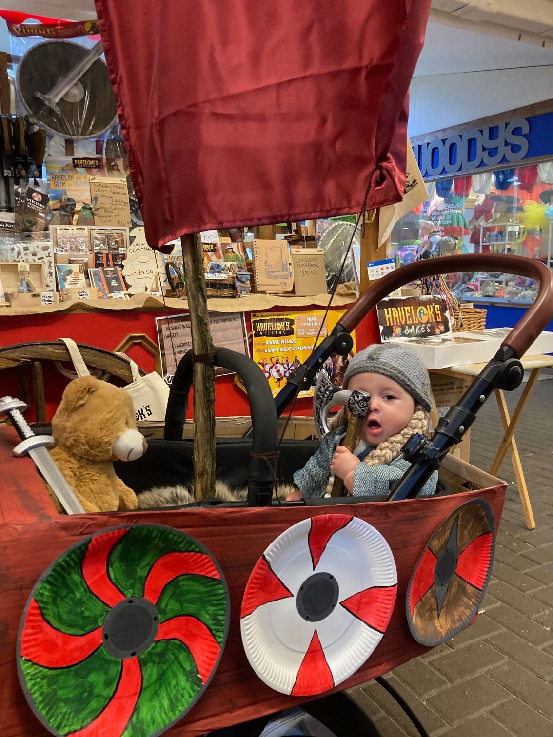 A baby is sitting in a stroller decorated to look like a viking ship.